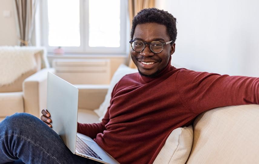 穿着红衬衫戴着眼镜的黑人坐在沙发上拿着笔记本电脑微笑着